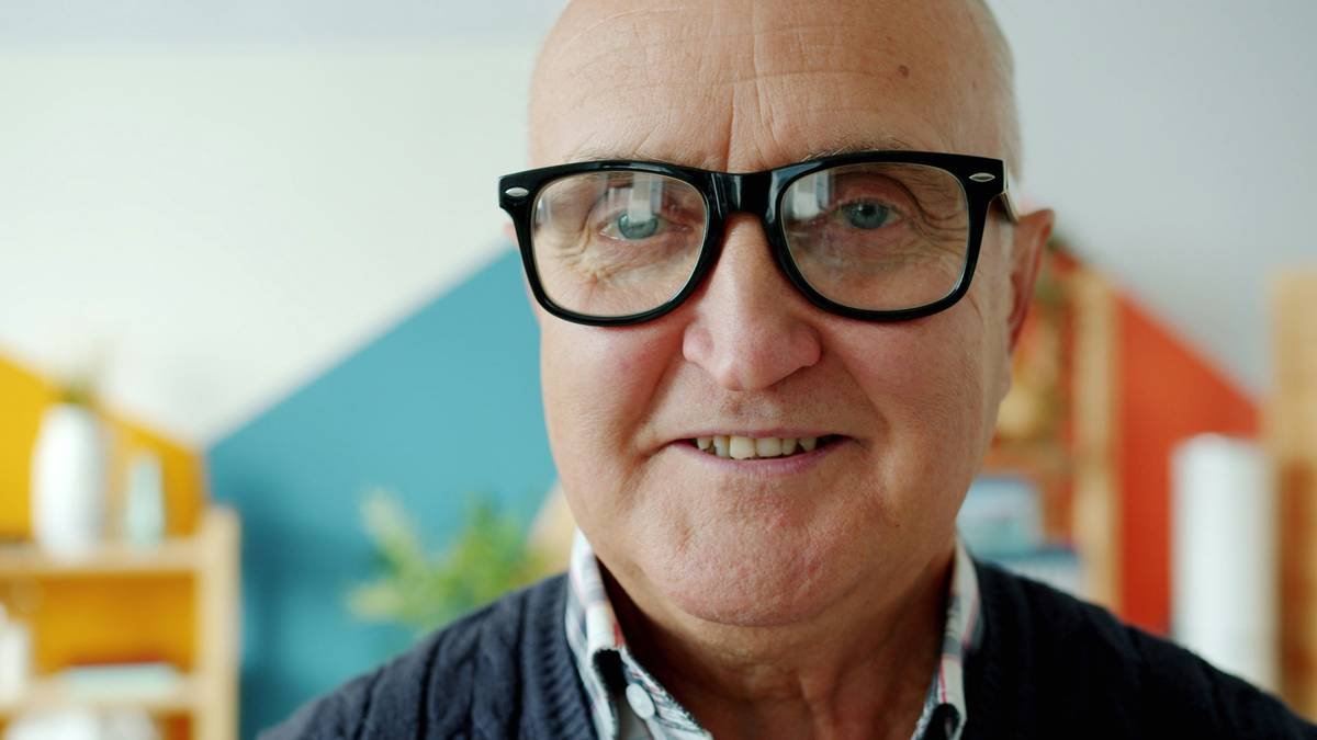 Close-up portrait of senior man in eyeglasses smiling looking at camera at home on bright background. Elderly people and positive emotions concept.