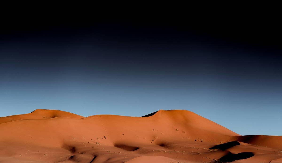 Desert sand dunes under a gradient blue sky