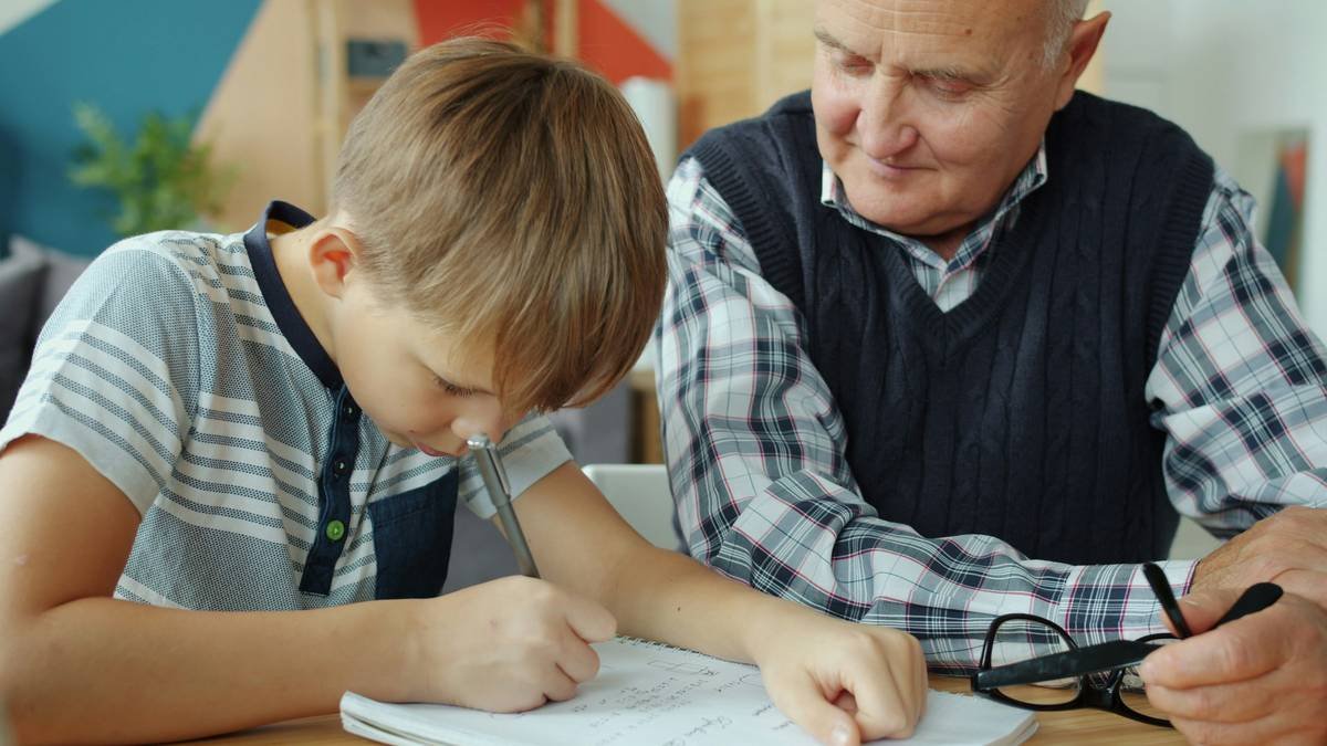 Grandson and grandfather are doing homework together at home then doing high-five, old man is showing thumbs-up. Happy loving family and education concept.