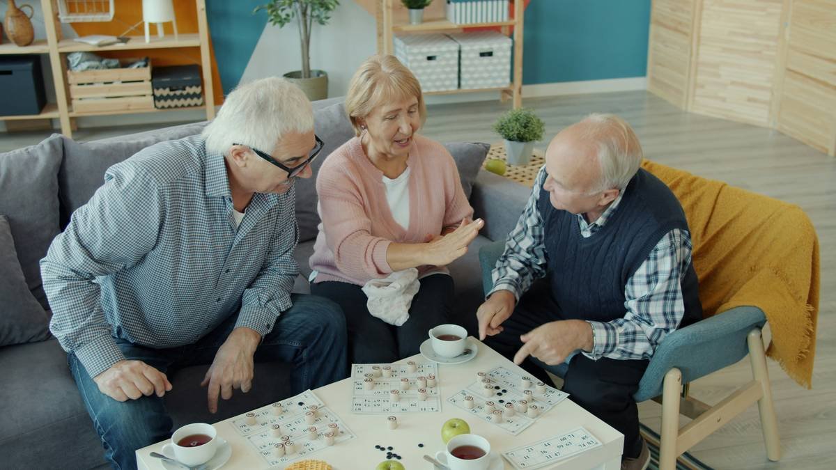 Old men and woman friends are playing lotto doing high-five showing thumbs-up in house. Board games, indoor entertainment and lifestyle concept.